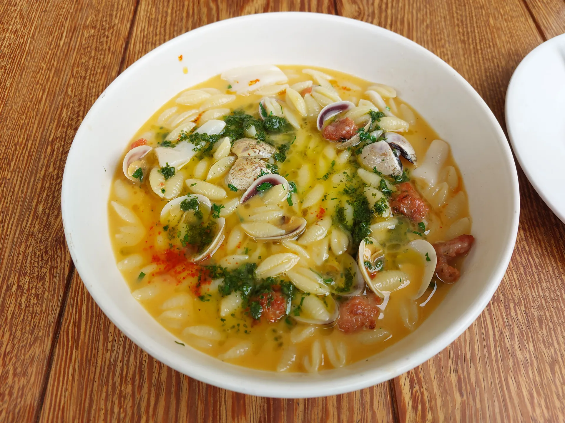 Seafood and shell pasta in a creamy ají-colored broth with clams, herbs, and a dusting of red spice.