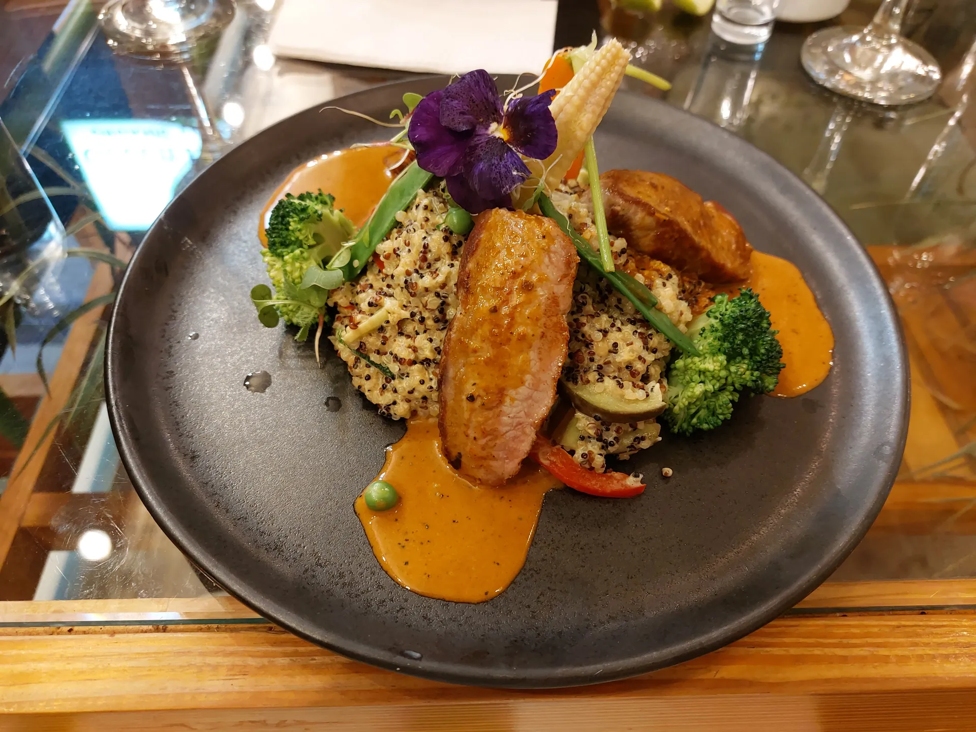 Seared alpaca medallions on tri-color quinoa with vegetables, aji amarillo sauce, and an edible flower.