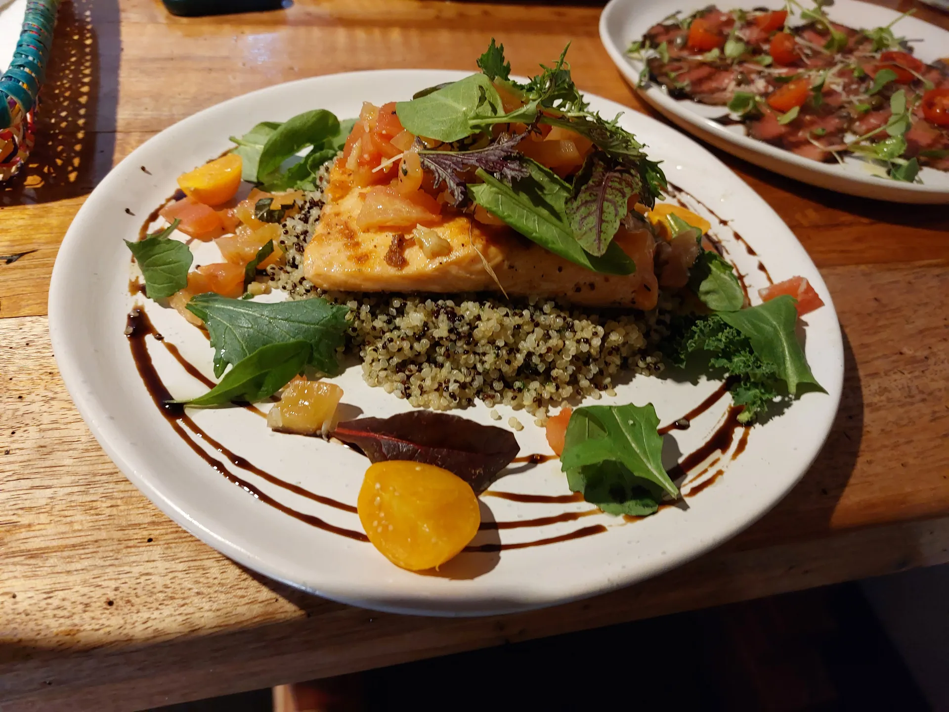 Pan-seared trout on quinoa with tomato salad; alpaca carpaccio on a second plate in the background.