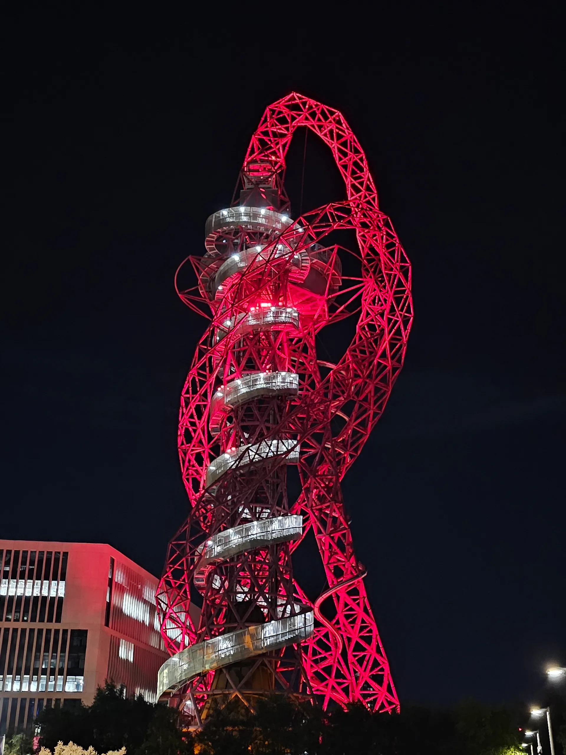 ArcelorMittal Orbit at night in Queen Elizabeth Olympic Park, red steel tower and lit spiral slide against a dark sky.